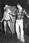 Two men dancing, one dressed as a female impersonator. thumbnail