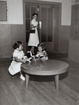 Two little girls sitting at a table playing while a woman watches thumbnail